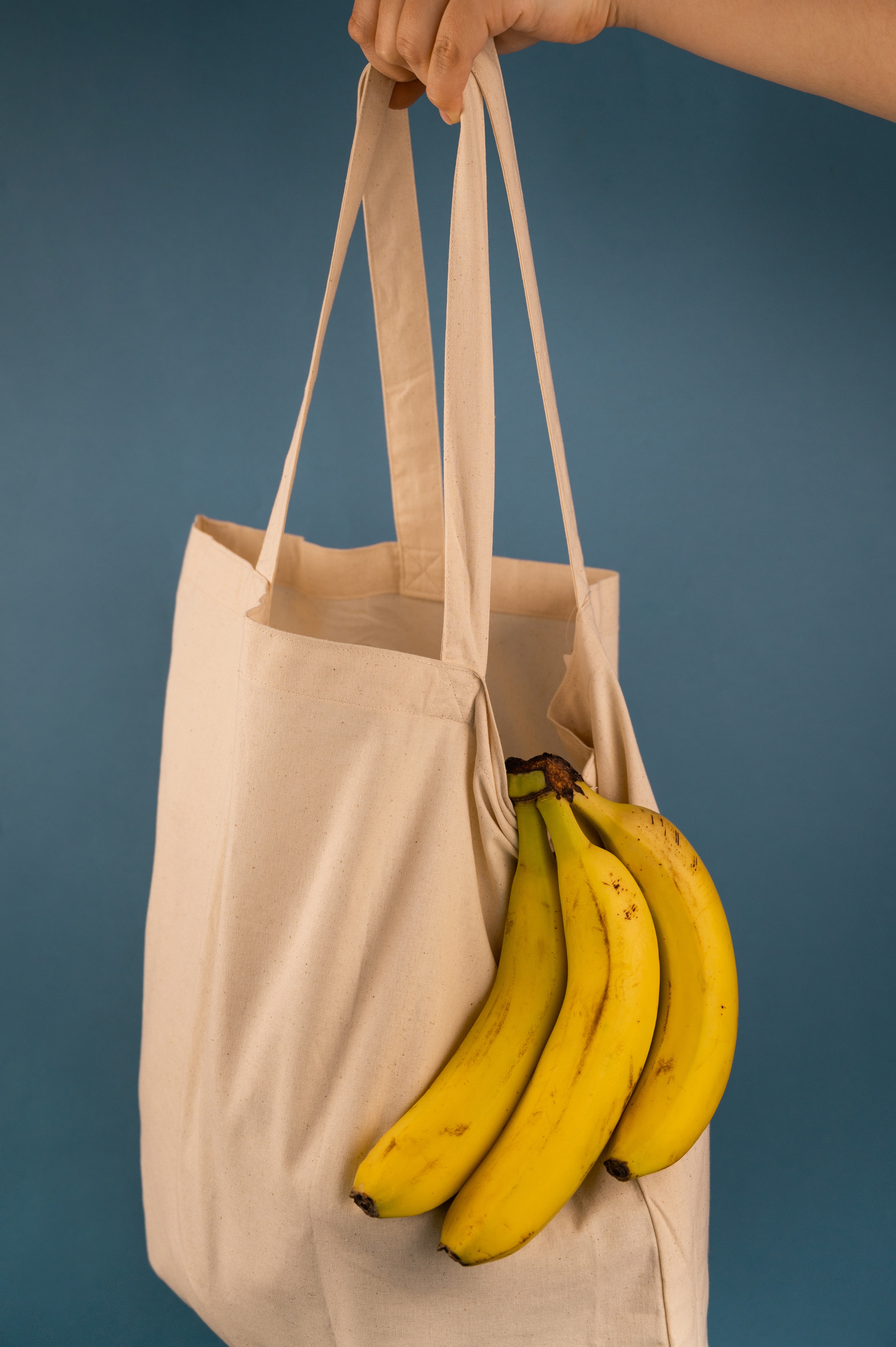 person holding reusable cloth bag with bananas