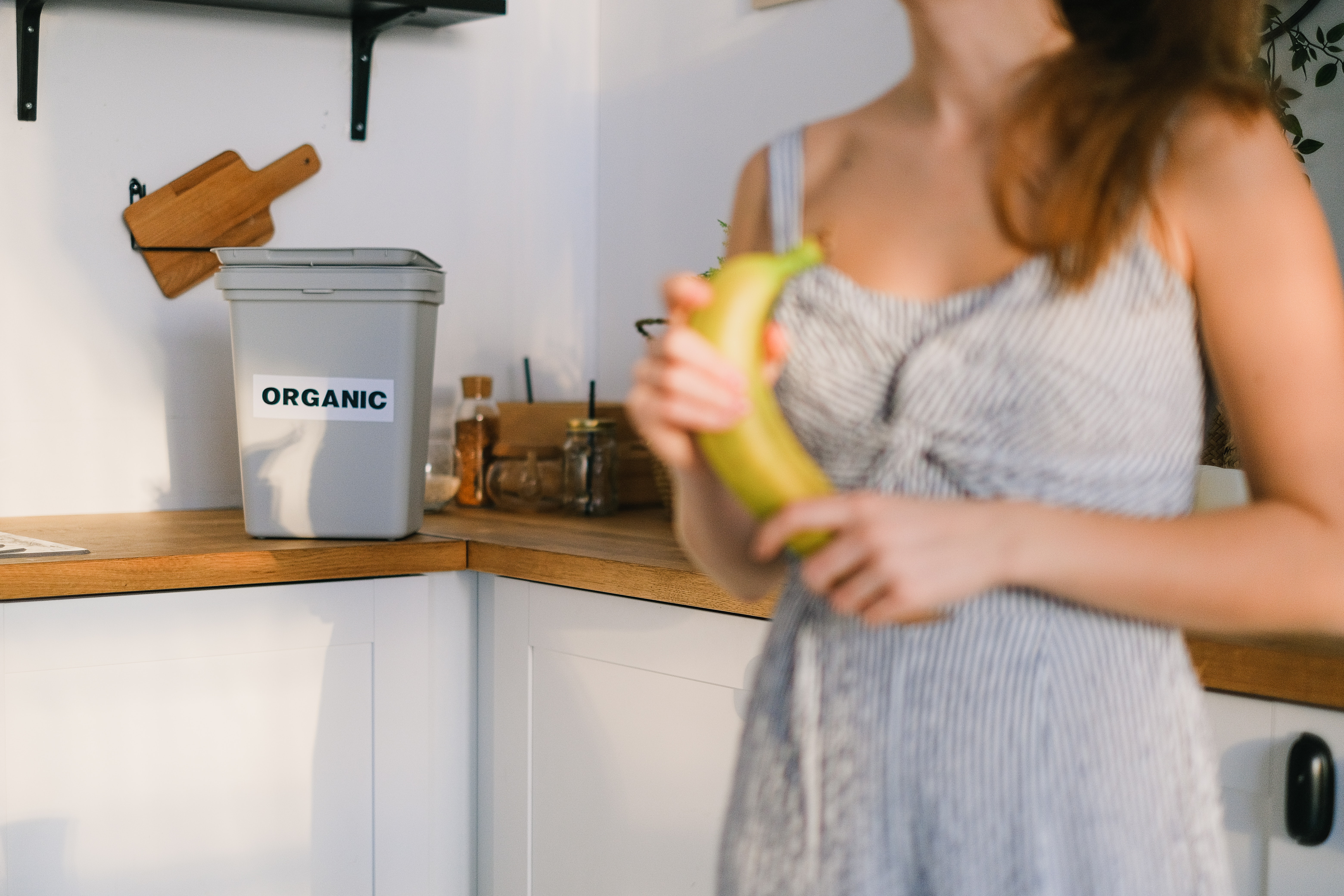 woman in kitchen holding a banana with an organic waste bin on the counter top