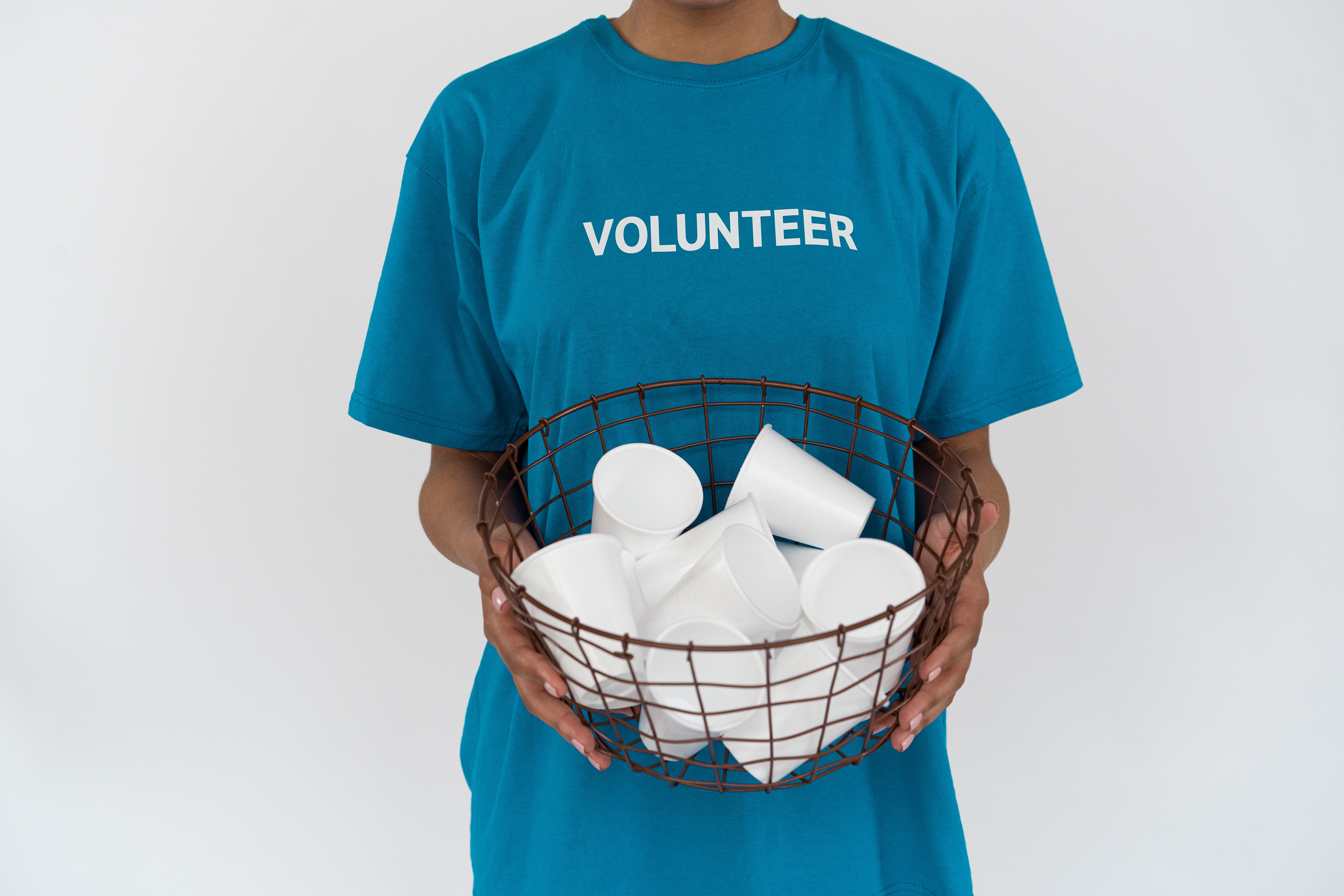 Person hold a basket of disposable cups with a t-shirt that says 'volunteer'